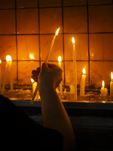 A hand lighting candles behind a window grid