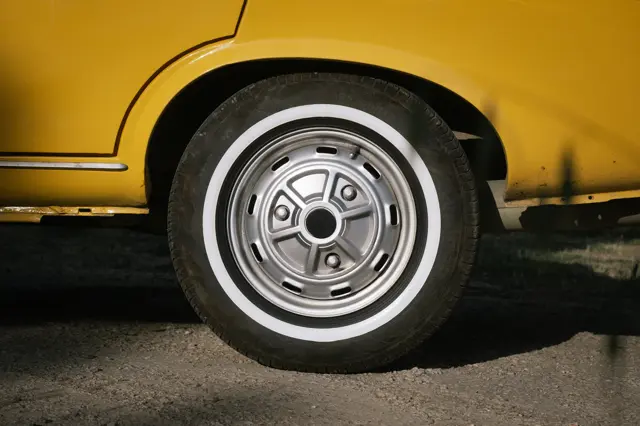 The wheel of a yellow classic car with a whitewall tyre