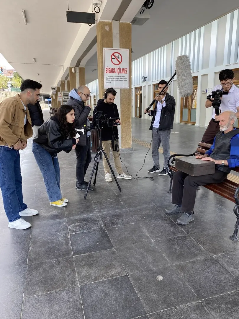 Film crew shooting an elderly man on a bench in a station