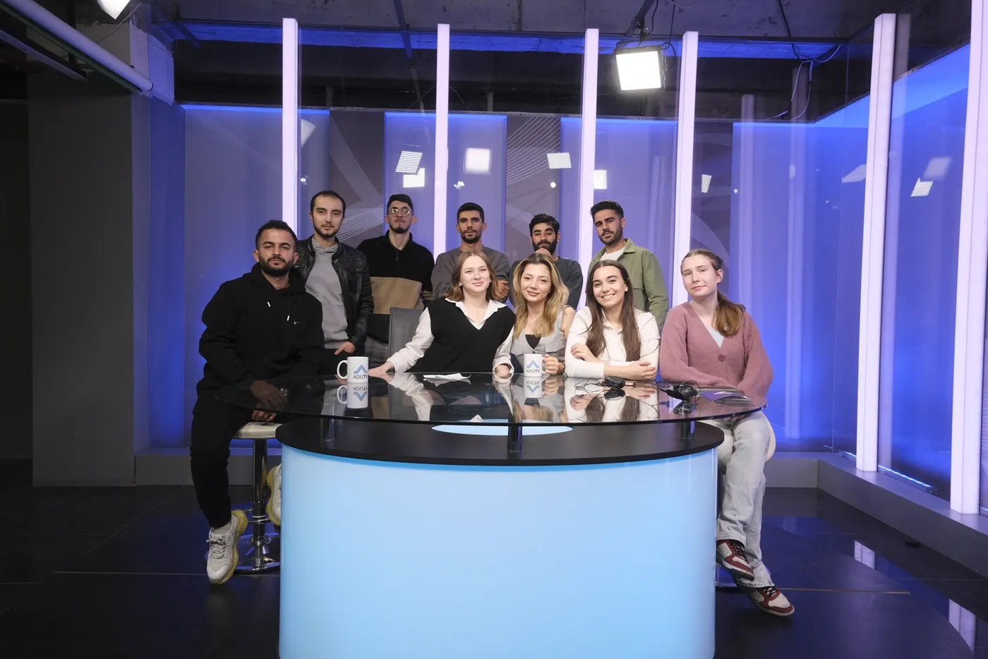 The crew together at a news desk in a television studio