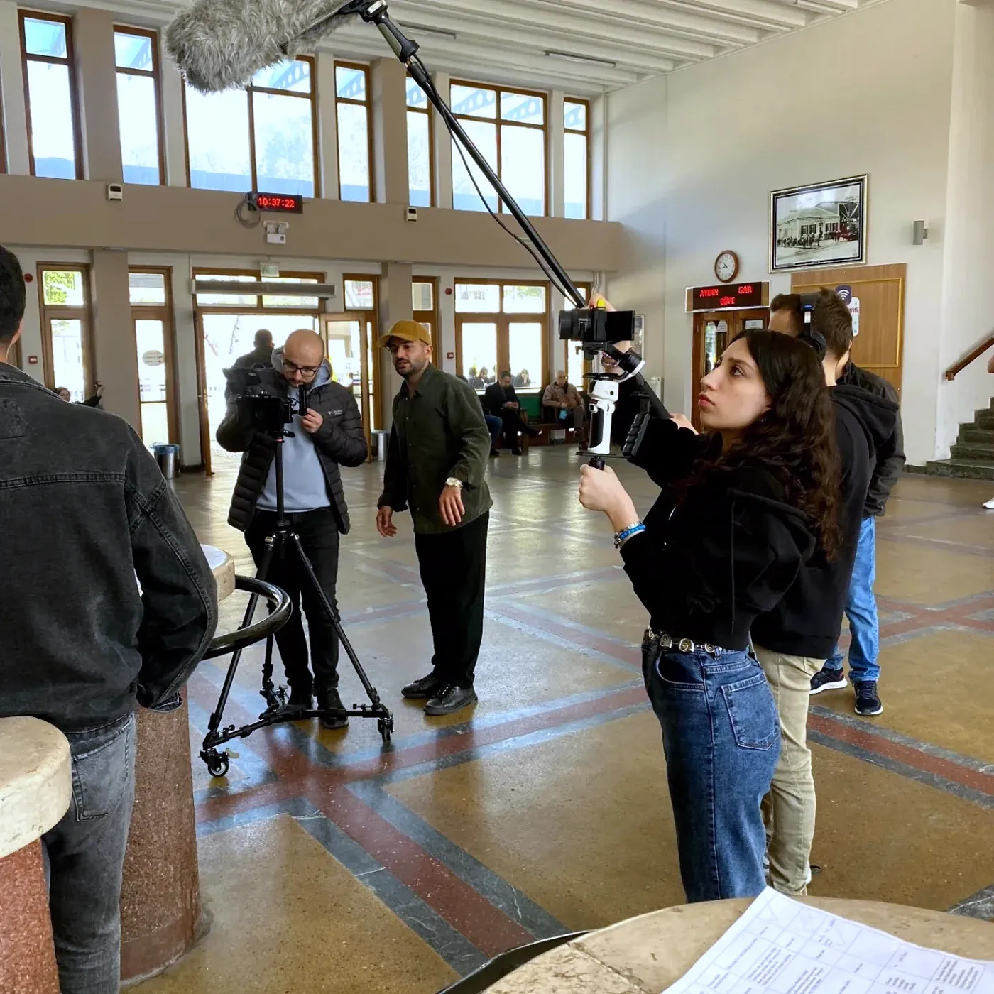 Crew shooting in the Aydın train station hall, a boom microphone overhead